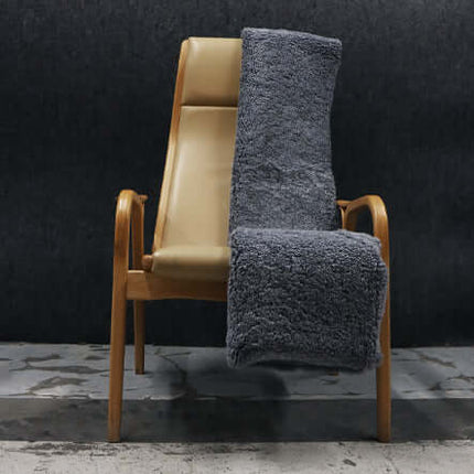 Luxe grijze schapenvacht gedrapeerd over een houten stoel, ideaal voor stijlvolle en knusse interieurdecoratie.