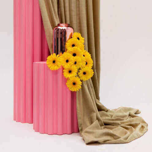 Gordijnstof Shift van Kendix met roze en groene tinten, elegant gedrapeerd naast felgele bloemen. Perfect voor verfijnd interieurontwerp.