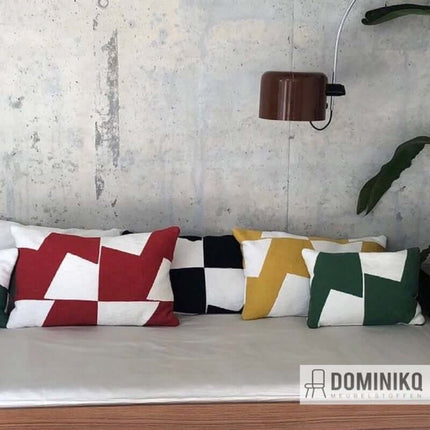 Kussens met grafisch patroon in rode, zwarte, gele en groene kleuren op een bank, gestyled met de Agape meubelstof collectie.