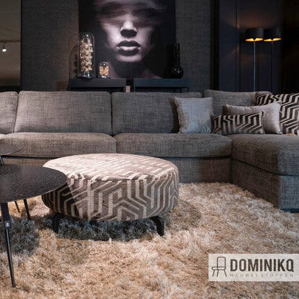 Moderne woonkamer met grijze hoekbank en ronde ottomaan, bekleed met Aristide Central Park jacquard velours meubelstof.
