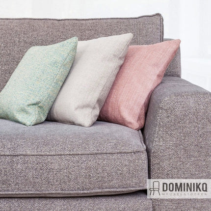 Grijze bank bekleed met Aristide meubelstof en drie kussens in pastelkleuren, behandeld met Aquaclean-technologie.