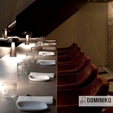 Moderne eetkamer met stijlvolle verlichting, met zachte fluwelen stoelen en gedekte tafel voorzien van glazen en servetten.