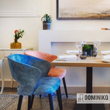 Luxe eetkamerstoel met fluwelen bekleding uit de Aristide Markle collectie, in de kleuren blauw en oranje, geplaatst aan een eettafel.