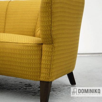 Detail van een gele bank bekleed met Bute Fabrics Ramshead stof, met een elegant Perzisch patroon en donkerhouten poten.
