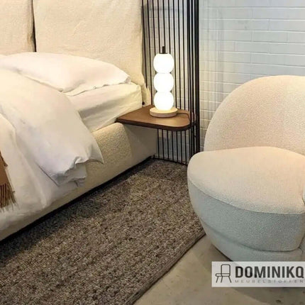 Moderne slaapkamer met zacht vloerkleed, comfortabele stoel en nachtkastje met lamp naast het bed.