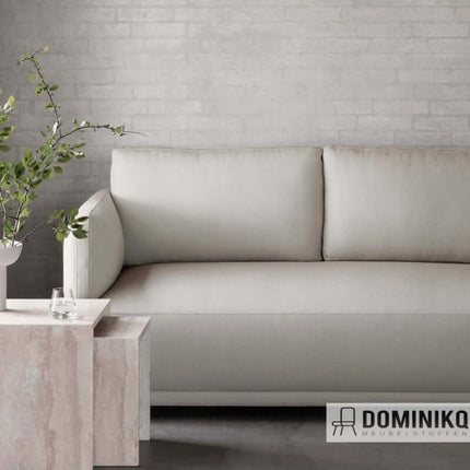 Stijlvolle bank bekleed met Kvadrat Sahco Ecriture stof in een moderne woonkamer, naast een marmeren tafel en groene plant