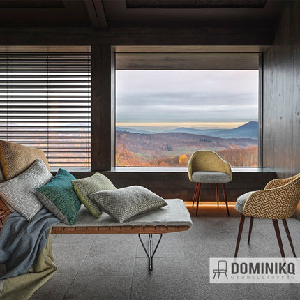 Moderne woonkamer met Casal Vertigo textiel op stoelen, uitzicht op landschap. Grijze, groene en gele tinten.