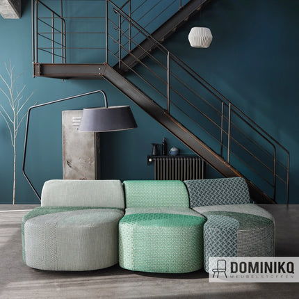 Stoffen bank bekleed met Casal's Garnier in groen en grijs patronen in een moderne woonkamer met metalen trap.