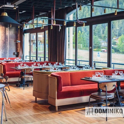 Moderne eetzaal met rood beklede stoelen, houten vloeren en grote ramen met uitzicht op de buitenomgeving.